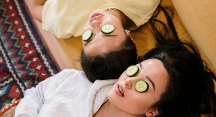 Two women enjoying a relaxing spa day with cucumber masks in a cozy home setting.